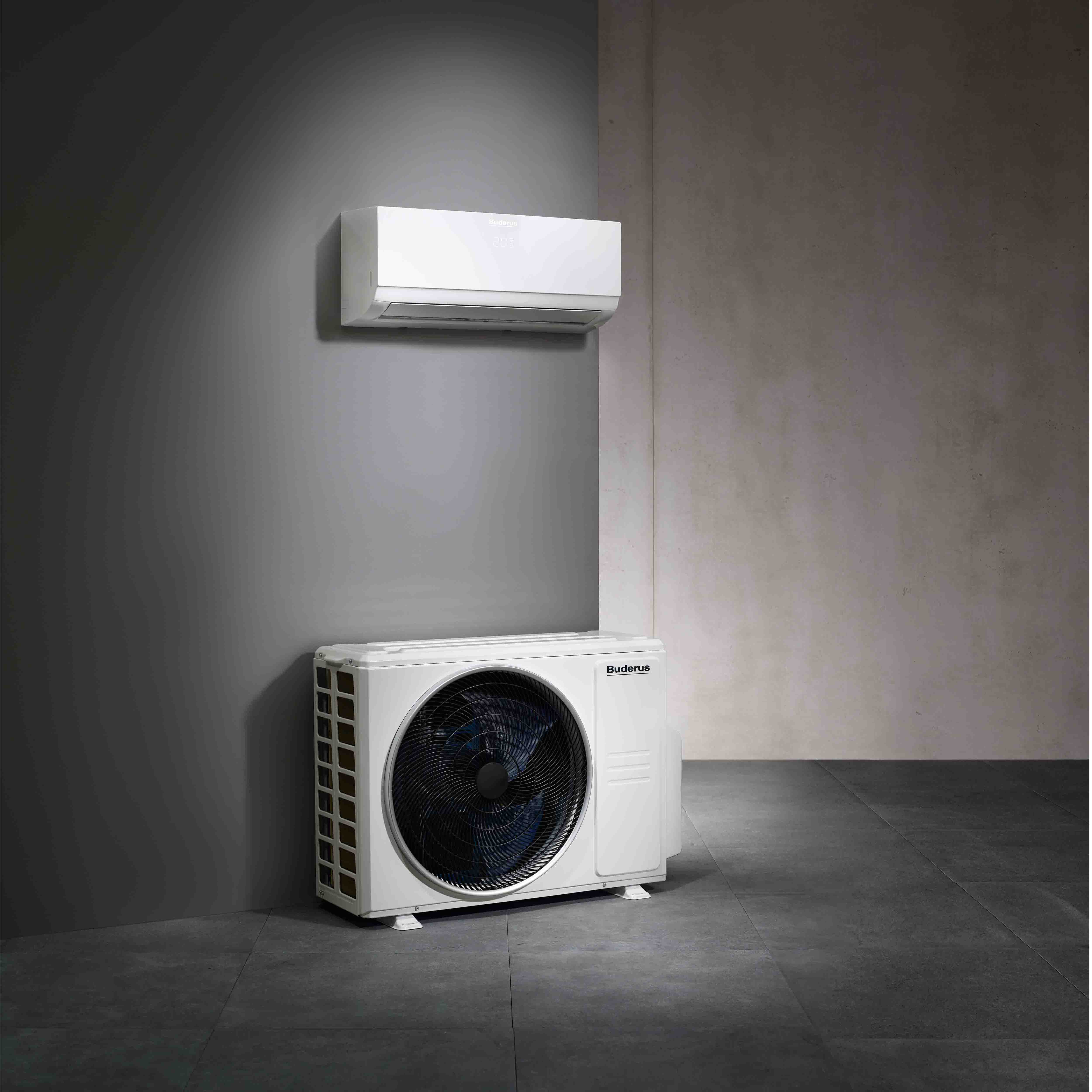 Ein modernes Split-Klimasystem mit einer wei&szlig;en Innenwandeinheit, die &uuml;ber einer passenden Au&szlig;enverfl&uuml;ssigereinheit auf einem gefliesten Boden vor grauen W&auml;nden montiert ist.