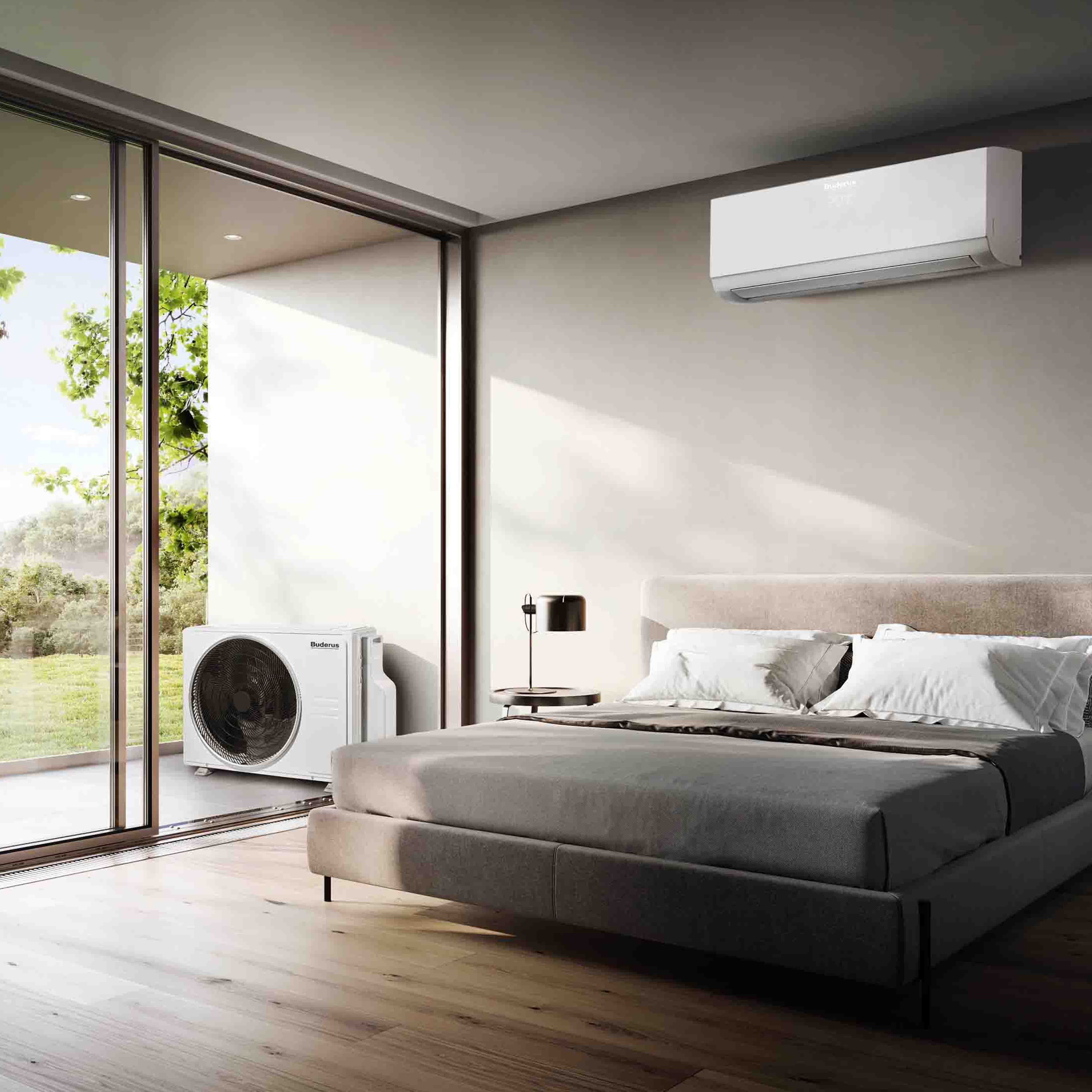 Modernes Schlafzimmer mit gro&szlig;em Bett, Nachttisch und Lampe, mit einer an der Wand montierten Klimaanlage &uuml;ber dem Bett und einem gro&szlig;en Fenster mit Blick ins Gr&uuml;ne.