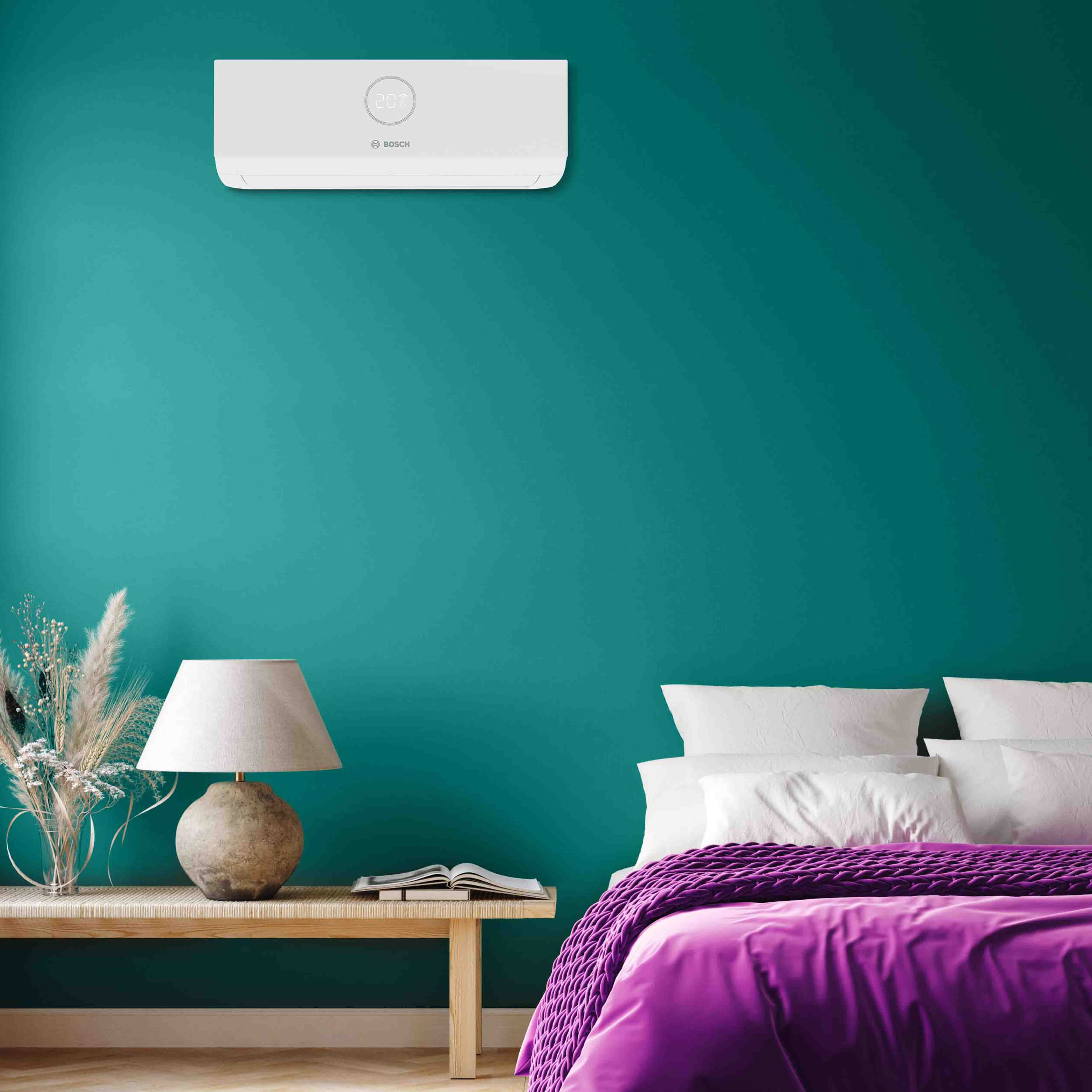 Ein modernes Schlafzimmer mit einer tealfarbenen Wand, einem Bett mit wei&szlig;en Kissen und einer lila Decke, einem Nachttisch mit einer Lampe, dekorativen Pflanzen und einem Buch sowie einer wei&szlig;en Klimaanlage &uuml;ber dem Bett.