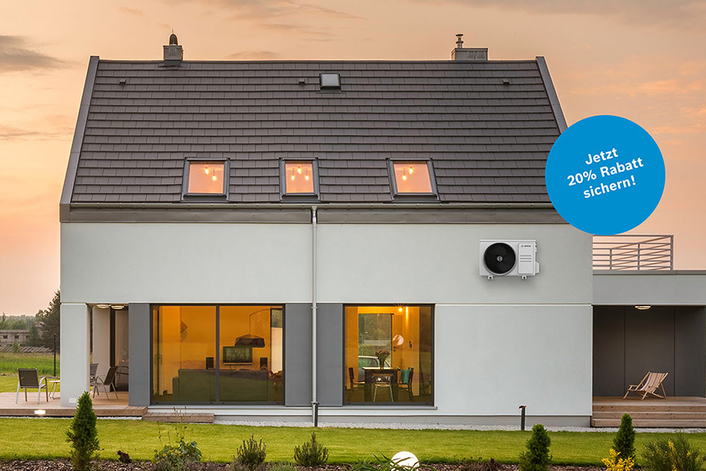 Modernes zweist&ouml;ckiges Haus mit gro&szlig;en Fenstern und einem schr&auml;gen Dach, das bei Sonnenuntergang innen warm beleuchtet ist. Ein blauer Kreis mit der Aufschrift 